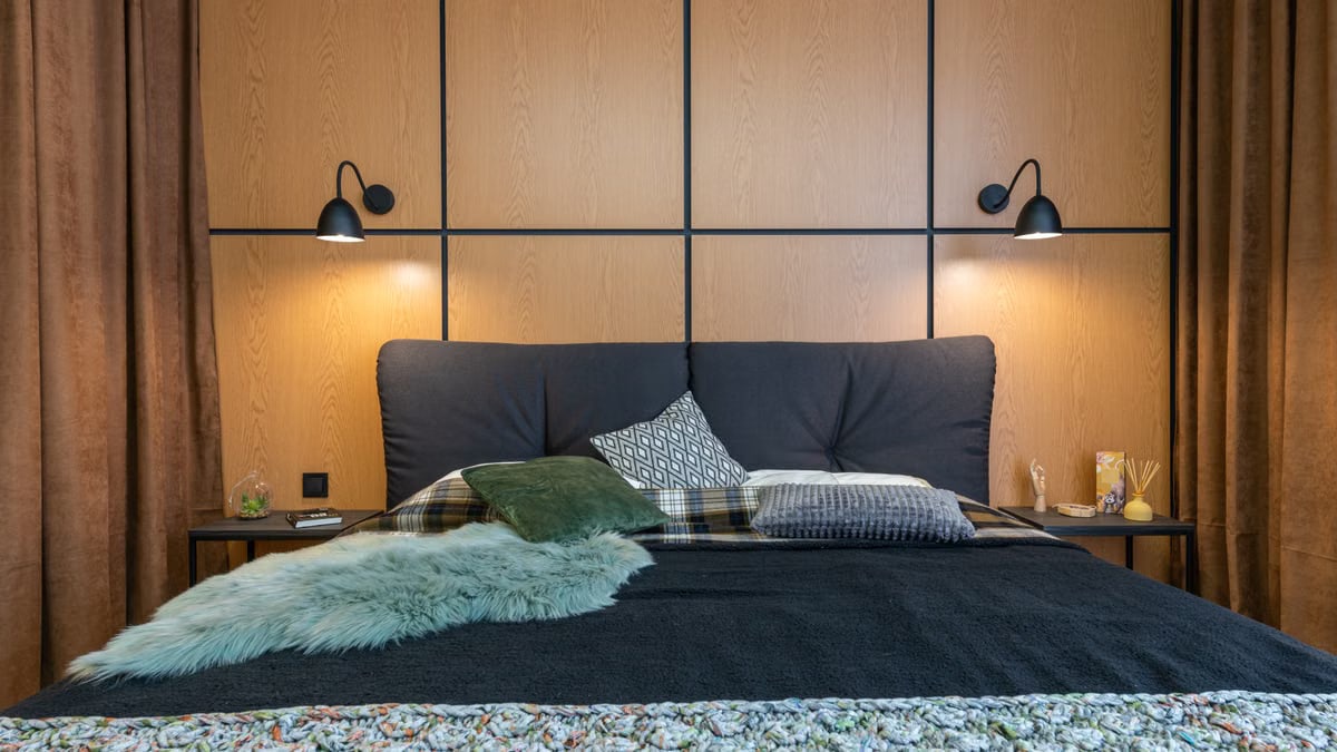 Comfortable big bed with soft cushions and bedside with aroma sticks under shining lamps hanging on wooden wall